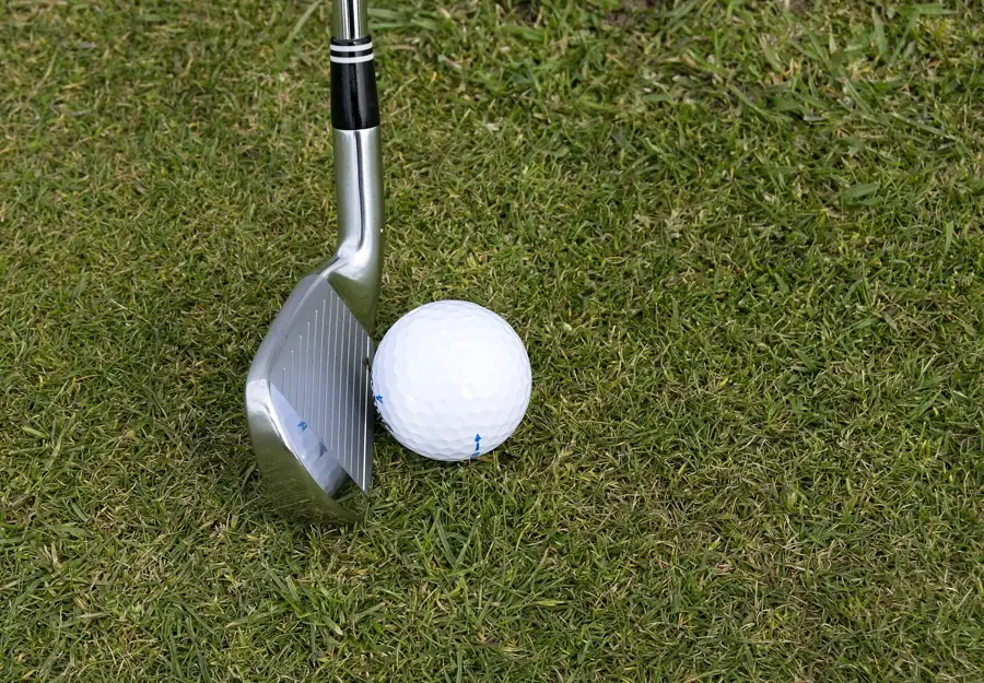 Tête d'un fer de golf posée derrière une balle sur le gazon du fairway