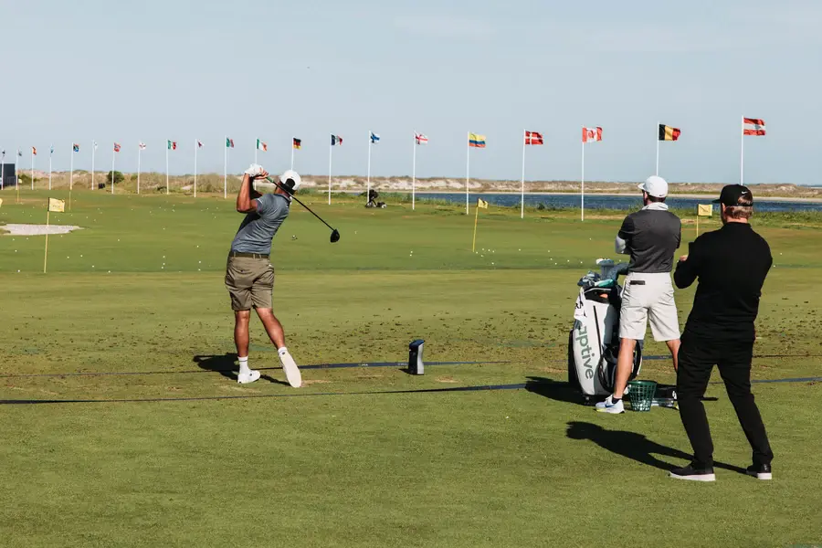 Golfeur terminant son swing au practice pendant que deux autres joueurs attendent derrière lui