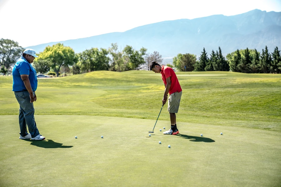 Deux golfeurs sur un green d'entraînement, l'un en train de putter, l'autre qui observe la ligne