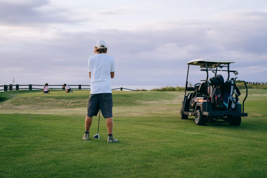Golfeur de dos sur un tee, regardant le fairway et le green au loin à côté d'une voiturette