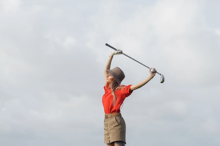 Golfeuse en polo rouge étirant les épaules avec un club tenu à bout de bras