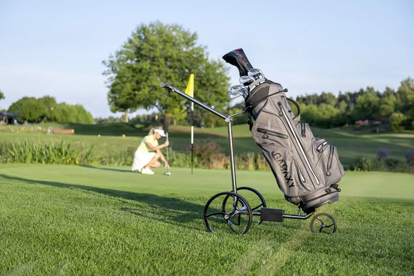 Chariot de golf électrique à trois roues portant un sac chargé, arrêté au bord d’un green